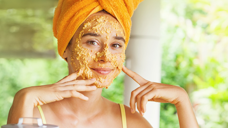 smiling woman with face mask treatment and hair wraped in towel