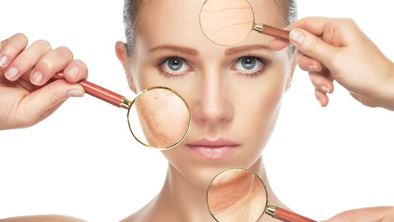 young womans healthy skin face, holding magnifiying glasses to show aging skin spots