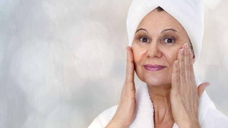 woman with white towel turban on head, white robe, hands on healthy face skin