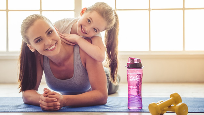 smiling mom with daughter on shoulders, water bottle and exercise equipment