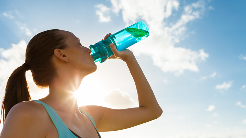 athletic woman drinking water with sky in back