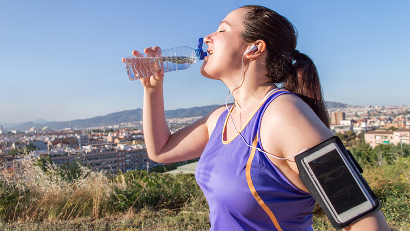 athletic woman drinking water with earbuds, city in back