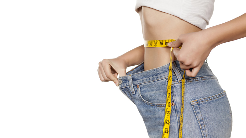 thin woman holding measuring tape on her waist, and holding pants out to show theyre too big