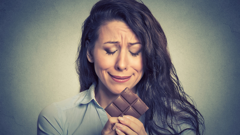 frowning woman holding chocolate as if she wants to eat it but shouldnt